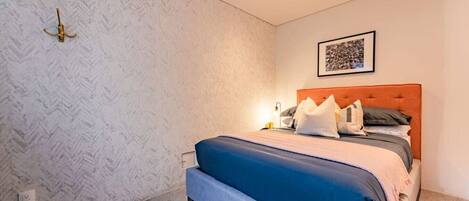 Une chambre à coucher avec un lit, une tête de lit, une lampe fixée au mur et un tableau encadré.