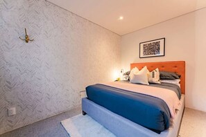 Ein Schlafzimmer mit einem Bett, einem Kopfteil, einer Wandleuchte und einem gerahmten Bild.