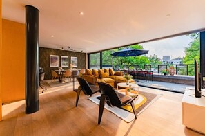 A modern living room with a sofa, chairs, and a dining area. There is a large window providing a view of the outdoors. - Polanco Penthouse: Rooftop Swing & City Views (Mexico City)