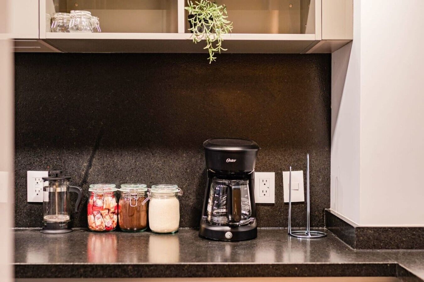 A kitchen counter with a coffee maker, jars of food, and a plant.