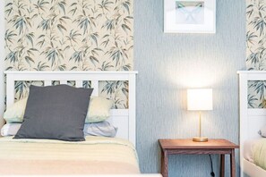 Ein Schlafzimmer mit einem Bett, Kissen, einem Nachttisch mit Lampe und einer Wand mit einem Bambusblattmuster.