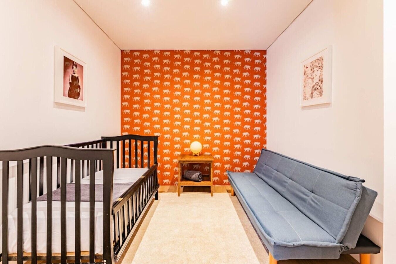 Een kamer met een ledikantje, een slaapbank, een klein tafeltje met een lamp en een kamer met een patroon op de muur.