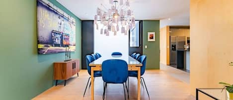 Un espace repas moderne avec une table en bois et des chaises bleues, un luminaire décoratif au plafond et une fresque colorée sur le mur.