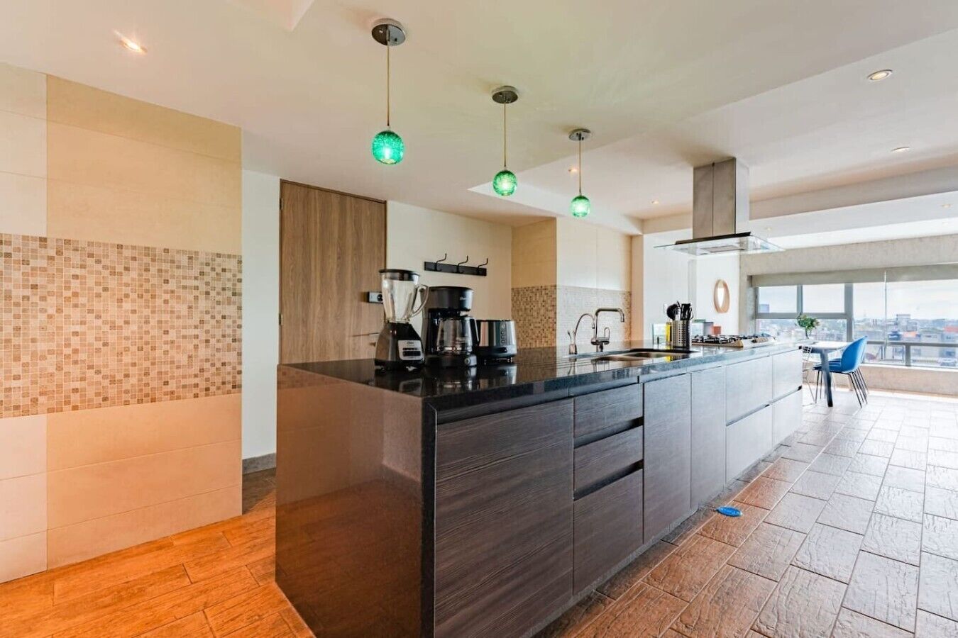 A modern kitchen with a central island, a coffee maker, and a view of the city through large windows.