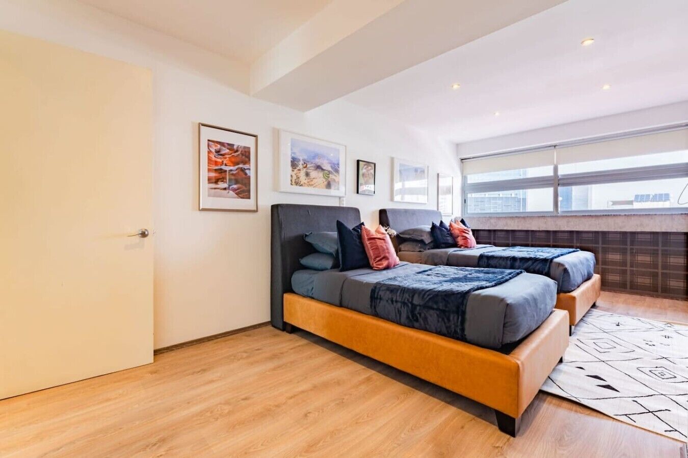 A modern bedroom with two beds, a large window, and artwork on the walls.