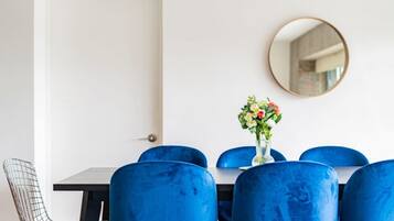 A dining area with a white door, a round mirror on the wall, and a table with blue chairs.