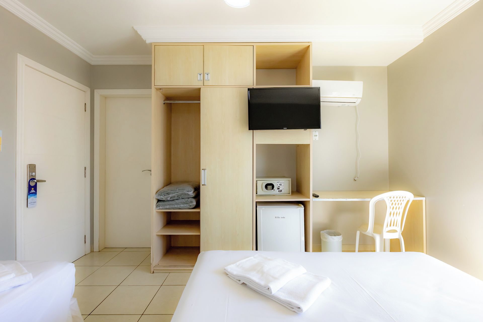 A hotel room with a bed, a desk, a TV, a wardrobe, and a small fridge.