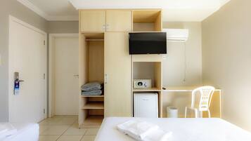 A hotel room with a bed, a desk, a TV, a wardrobe, and a small fridge.