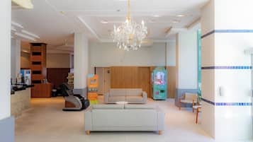 A modern lobby with a chandelier, a reception desk, a sofa, and a claw machine.