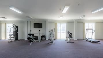 A spacious gym with various exercise equipment, large windows, and a flat-screen TV on the wall.