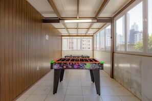 Una habitación con mesa de fútbol, paredes de madera y ventana con vista a la ciudad.