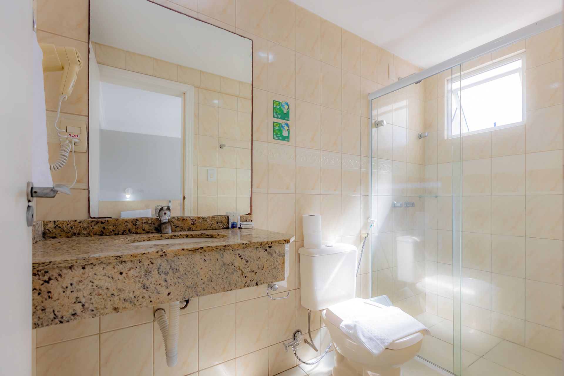 A bathroom with a granite countertop, a toilet, a glass-enclosed shower, and a mirror.