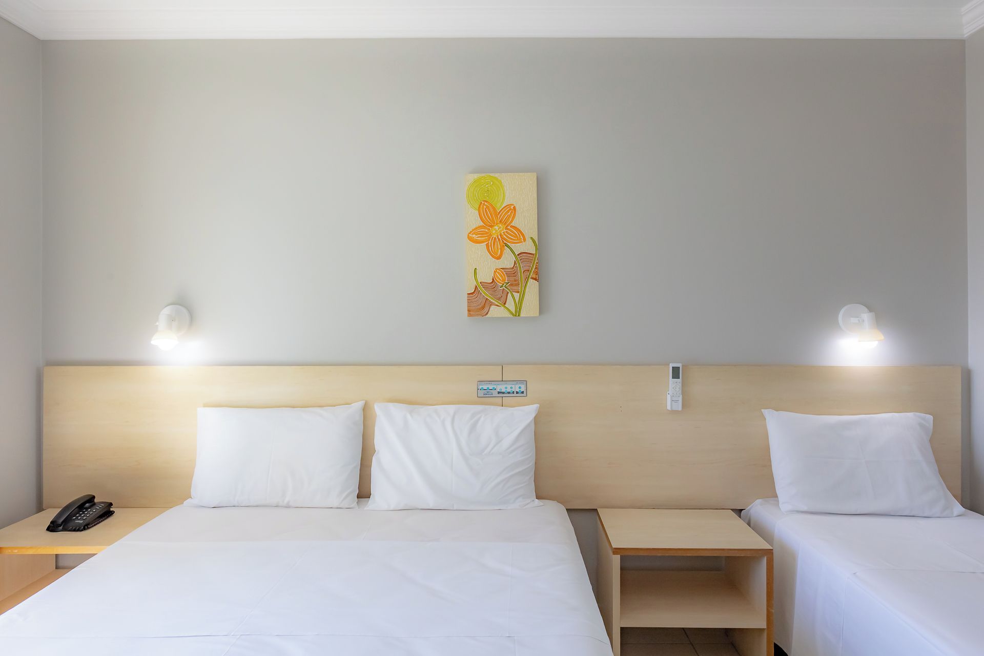 A hotel room with a bed, two bedside tables, a wall-mounted phone, and a wall art piece.