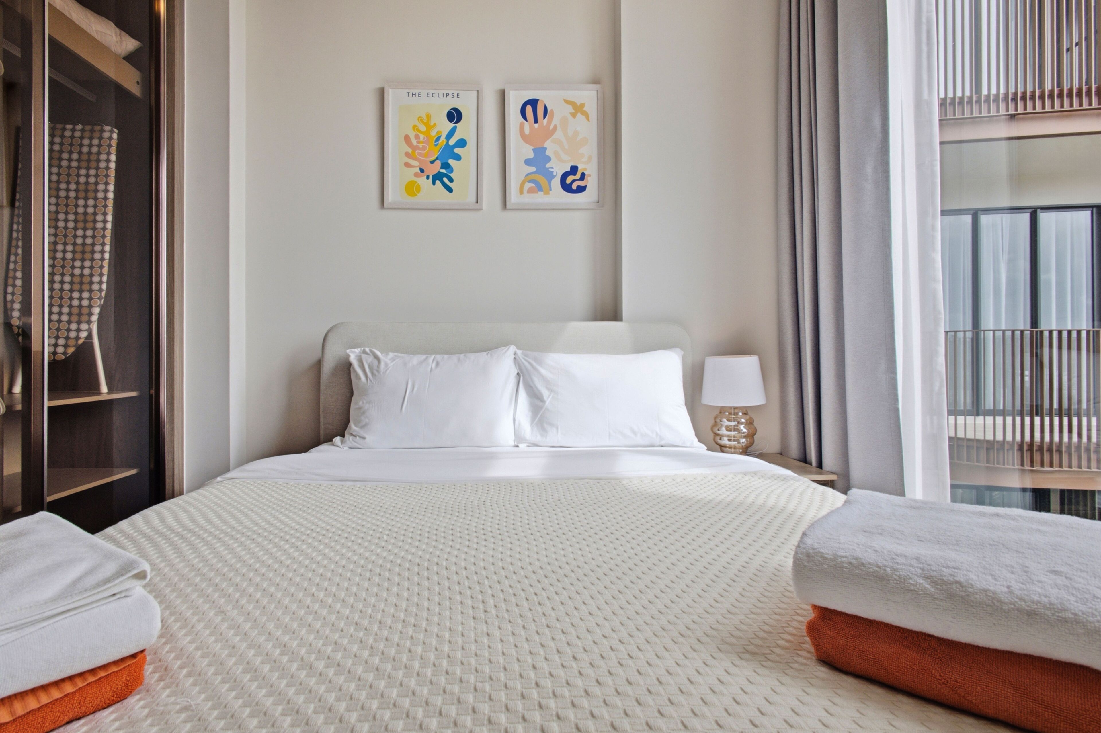 Habitación de hotel con una cama grande, dos almohadas, una mesita de noche con una lámpara y dos cuadros enmarcados en la pared.