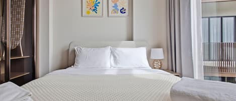 Habitación de hotel con una cama grande, dos almohadas, una mesita de noche con una lámpara y dos cuadros enmarcados en la pared.