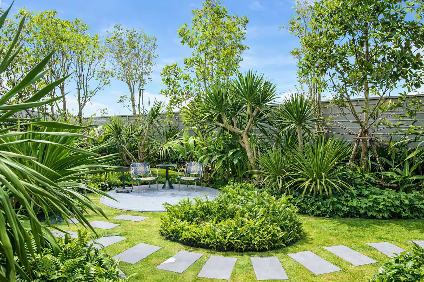 Een tuin met een ronde zithoek, omringd door verschillende planten en bomen.