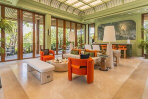 Eine geräumige Lobby mit hoher Decke, großen Fenstern und einer Sitzecke mit orangefarbenen Stühlen und einem weißen Sofa.