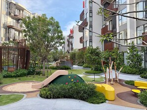 Un edificio residencial con varios balcones, un área de juegos con un tobogán y un jardín cuidado.