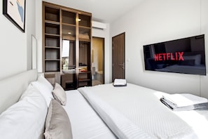 Una habitación de hotel con cama, televisor montado en la pared, armario y escritorio.
