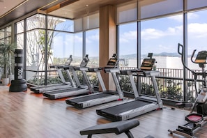 Un gimnasio con cintas de correr, un saco de boxeo y vistas de la ciudad a través de amplias ventanas.