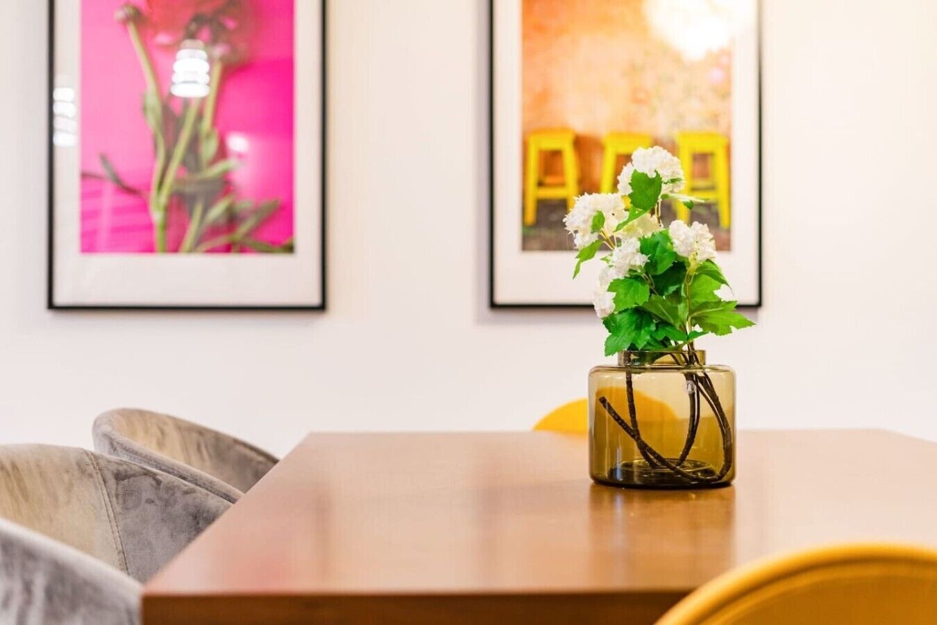 Une table en bois sur laquelle se trouve un vase en verre contenant des fleurs blanches et des feuilles vertes.