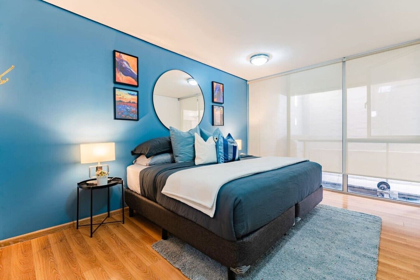 Une chambre à coucher avec un lit, un miroir rond et des œuvres d’art accrochées au mur.