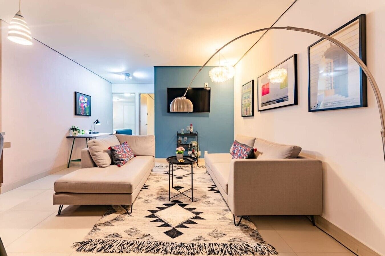 Un salon moderne avec deux canapés, une table basse et un téléviseur. Les murs sont ornés de tableaux encadrés, et un luminaire au design original et aux formes courbes complète l’ensemble.
