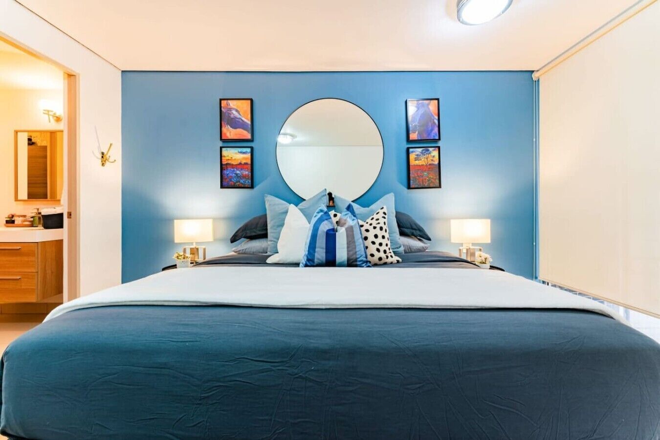 A hotel room with a large bed, a round mirror, and artwork on the walls.
