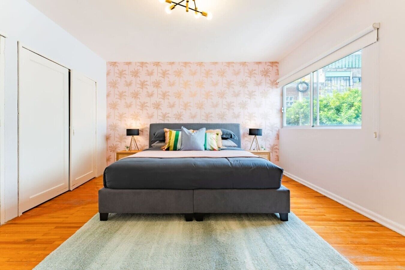 A bedroom with a large bed, two bedside lamps, a window with a view, and a patterned wallpaper.
