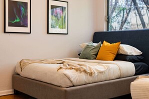 Een slaapkamer met een bed, kussens en twee afbeeldingen in een lijst aan de muur.