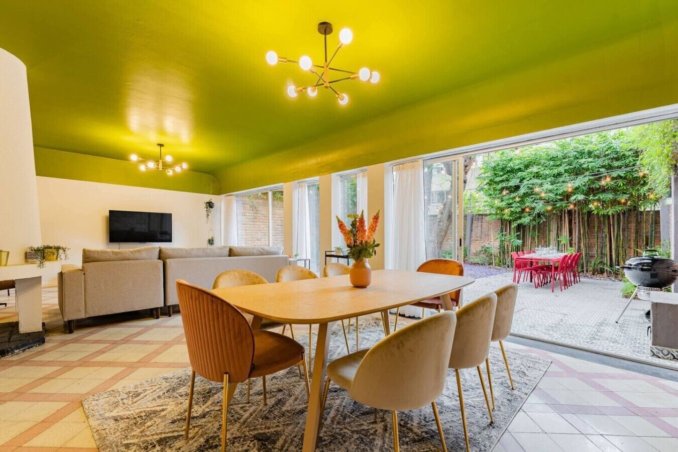 A modern living space with a dining area, a sofa, a TV, and a view of a garden.