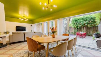 A modern living space with a dining area, a sofa, a TV, and a view of a garden.