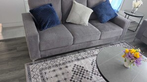 A grey upholstered sofa with a patterned rug and a small round table with a vase of flowers.