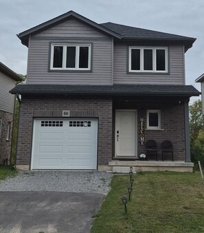 A two-story house with a garage, a front door, and a welcome sign.