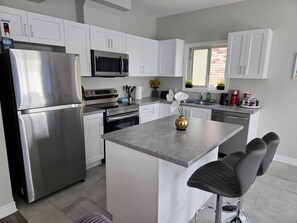 A modern kitchen with white cabinets, stainless steel appliances, and a central island with bar stools.