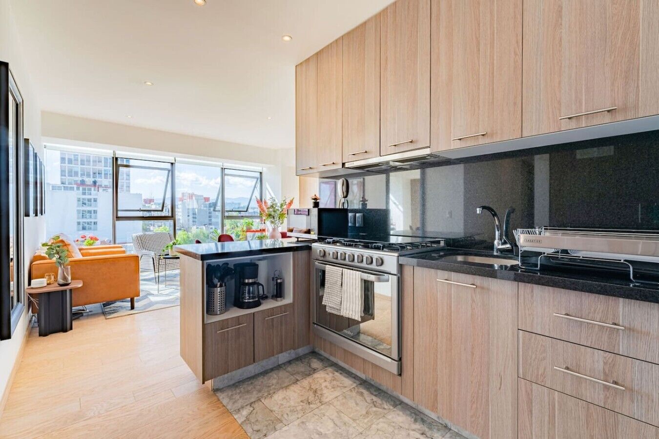 A modern kitchen with wooden cabinets, a built-in oven, and a large window overlooking a cityscape.