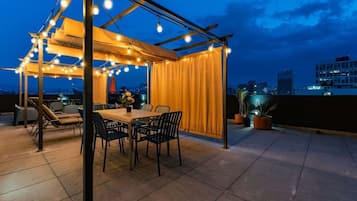 An outdoor patio with a table and chairs, string lights, and potted plants.