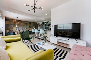 A modern living room with a large flat-screen TV, a yellow sofa, and a dining area with chairs and a kitchen in the background. - Private Terrace Escape in the Heart of Roma Norte (Mexico City)