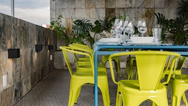 Een terras met een tafel gedekt voor vier personen, omringd door gele stoelen, met een stenen muur op de achtergrond.
