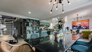 Een moderne keuken met een eethoek, met een glazen tafel, rieten stoelen en blauwgroene kastjes.
