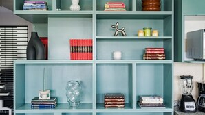 Een blauwgroene boekenkast met diverse spullen, waaronder boeken, een decoratief beeldje en een blender.