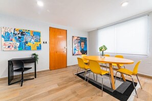 A room with a wooden floor, a round yellow table with four chairs, a black desk with a chair, and two large abstract paintings on the walls. - Roma Norte Stay • Pet Friendly, Walk to Cafés (Mexico City)