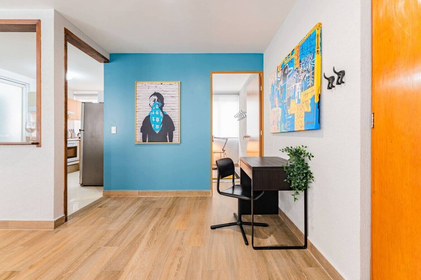 A hallway with a blue wall, a wooden floor, a desk with a chair, and a plant.