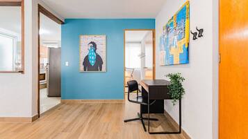 A hallway with a blue wall, a wooden floor, a desk with a chair, and a plant.