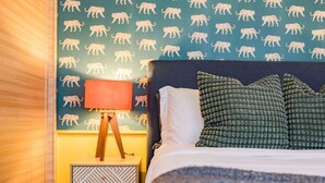Et hotelværelse med en seng, puder, et natbord, en lampe og en væg med dyremotiver.