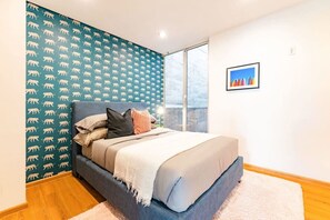 A bedroom with a bed, pillows, a blanket, a window, and a wall with a pattern. - 2 Condos in La Roma | Parking, Perfect for Groups (Mexico City)