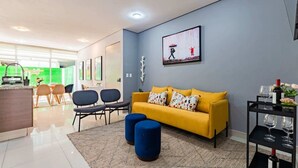 A modern living room with a yellow sofa, blue ottomans, and a dining area with chairs and a table. - 2 Condos in La Roma | Parking, Perfect for Groups (Mexico City)