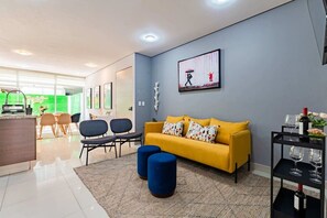 Ein modernes Wohnzimmer mit einem gelben Sofa, blauen Hocker und einem Essbereich mit Stühlen und einem Tisch.