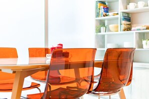 A dining area with a wooden table and orange chairs, a bookshelf in the background, and a window providing natural light. - 2 Condos in La Roma | Parking, Perfect for Groups (Mexico City)