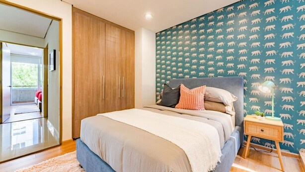A bedroom with a bed, a nightstand, a wall with a pattern, and a door leading to another room. - 2 Condos in La Roma | Parking, Perfect for Groups (Mexico City)